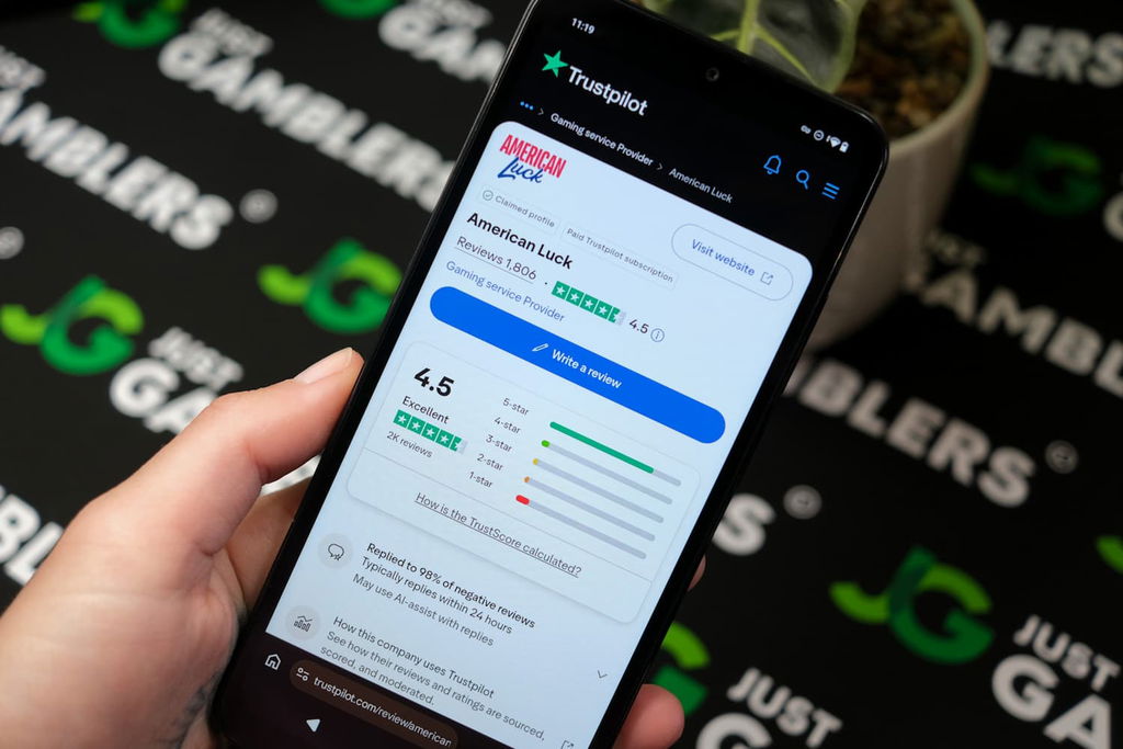 Angela Zillich holding an Android Phone with the American Luck casino Trustpilot ratings page loaded on the webpage.