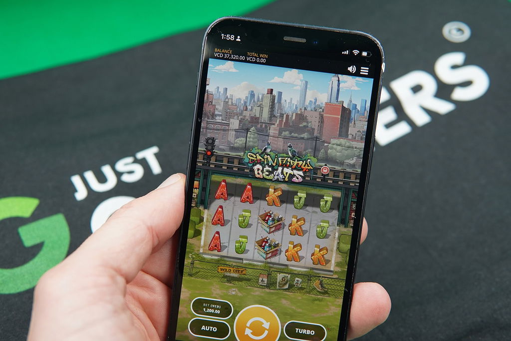 Patrik Lidin holding an iPhone with BananaBets casino game Spin City Beats showing.