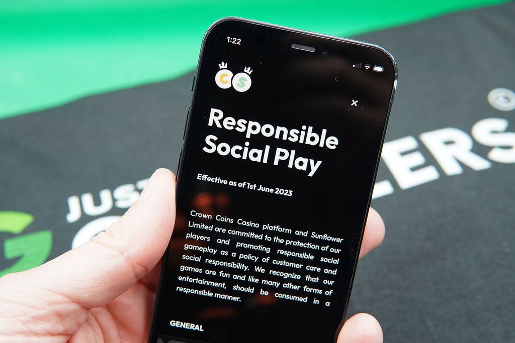 Patrik Lidin holding an iPhone with the Crown Coins Casino responsible gambling page showing.