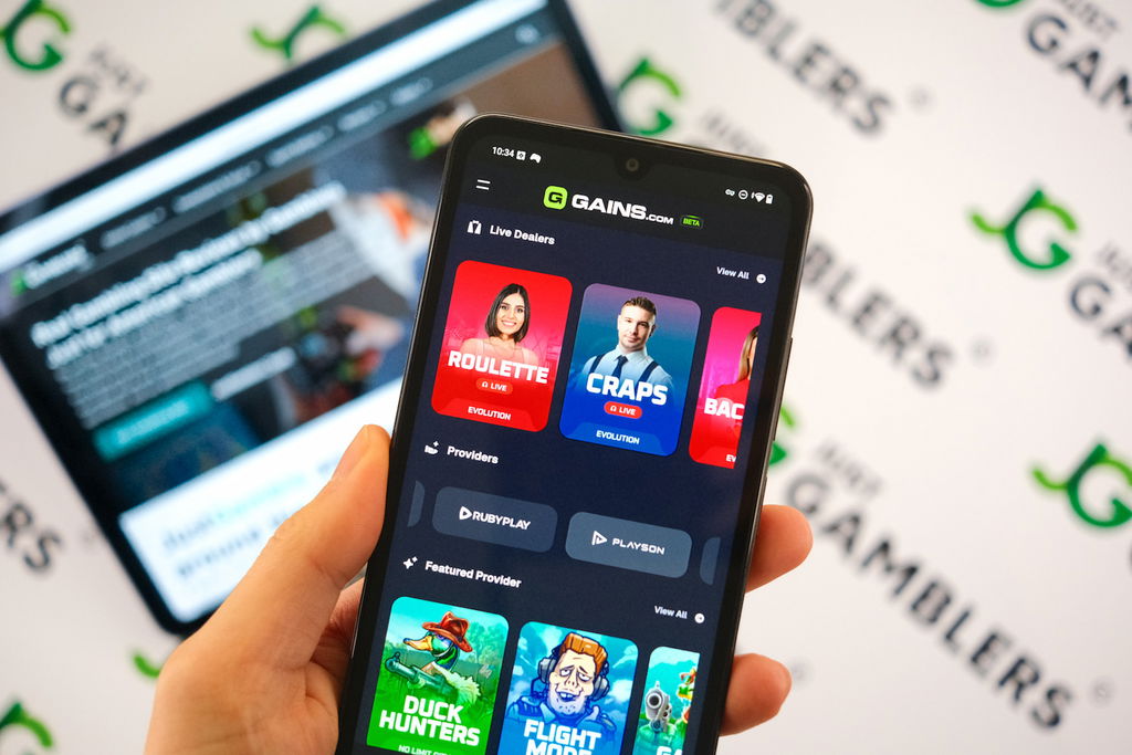 Angela Zillich holding an Android Phone with the Gains casino game lobby page loaded on the webpage.
