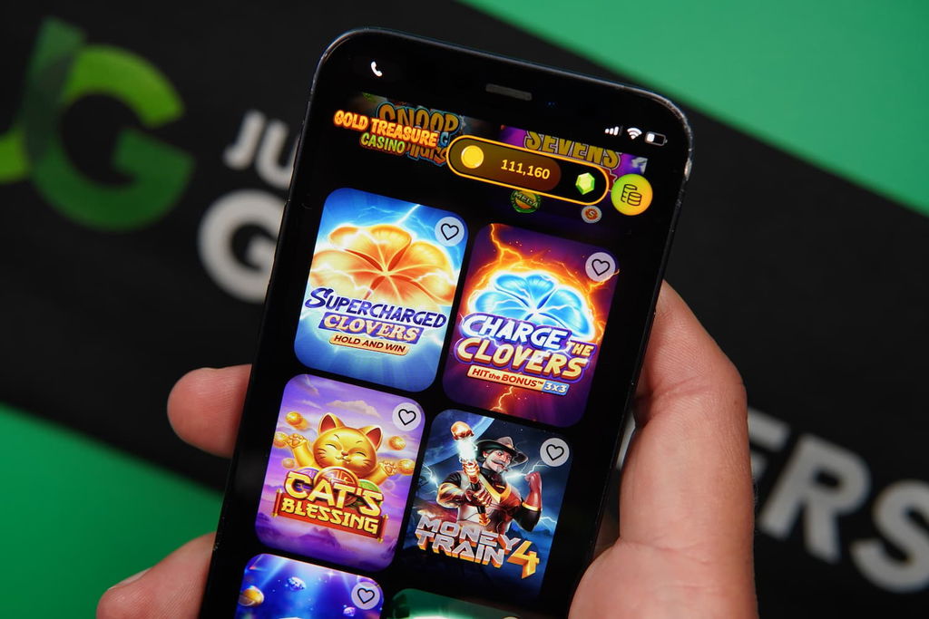 Patrik Lidin holding an iPhone with the Gold Treasure casino game library page loaded on the webpage.