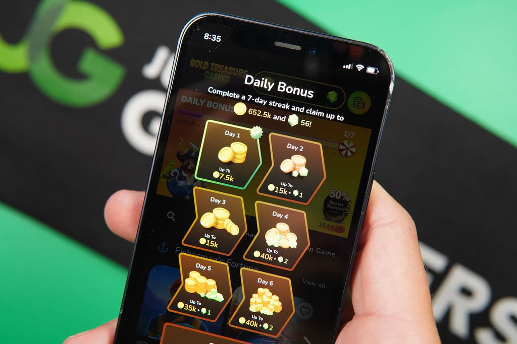 Patrik Lidin holding an iPhone with the Gold Treasure casino Promotions page loaded on the webpage.