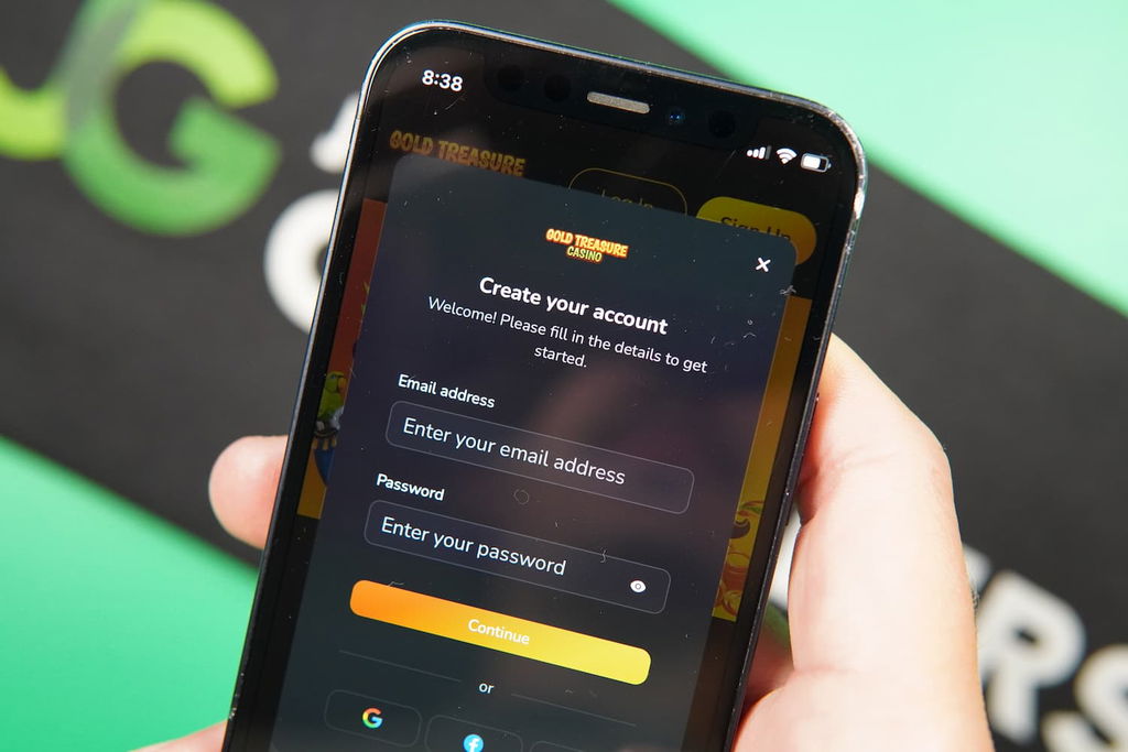 Patrik Lidin holding an iPhone with the Gold Treasure casino Registration page loaded on the webpage.