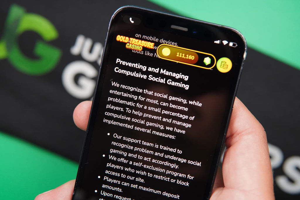 Patrik Lidin holding an iPhone with the Gold Treasure casino Responsible Gaming page loaded on the webpage.