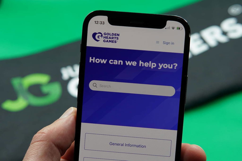Patrik Lidin holding an iPhone with the Golden Hearts Games casino support page loaded on the webpage.