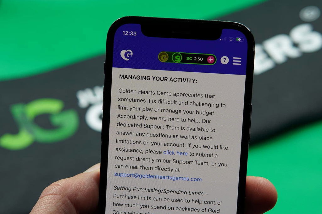 Patrik Lidin holding an iPhone with the Golden Hearts Games casino responsible gambling page loaded on the webpage.