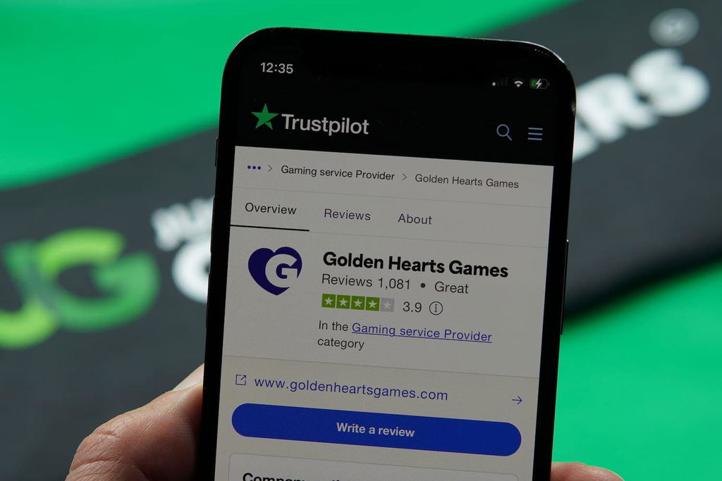 Patrik Lidin holding an iPhone with the Golden Hearts Games casino Trustpilot rating loaded on the webpage.