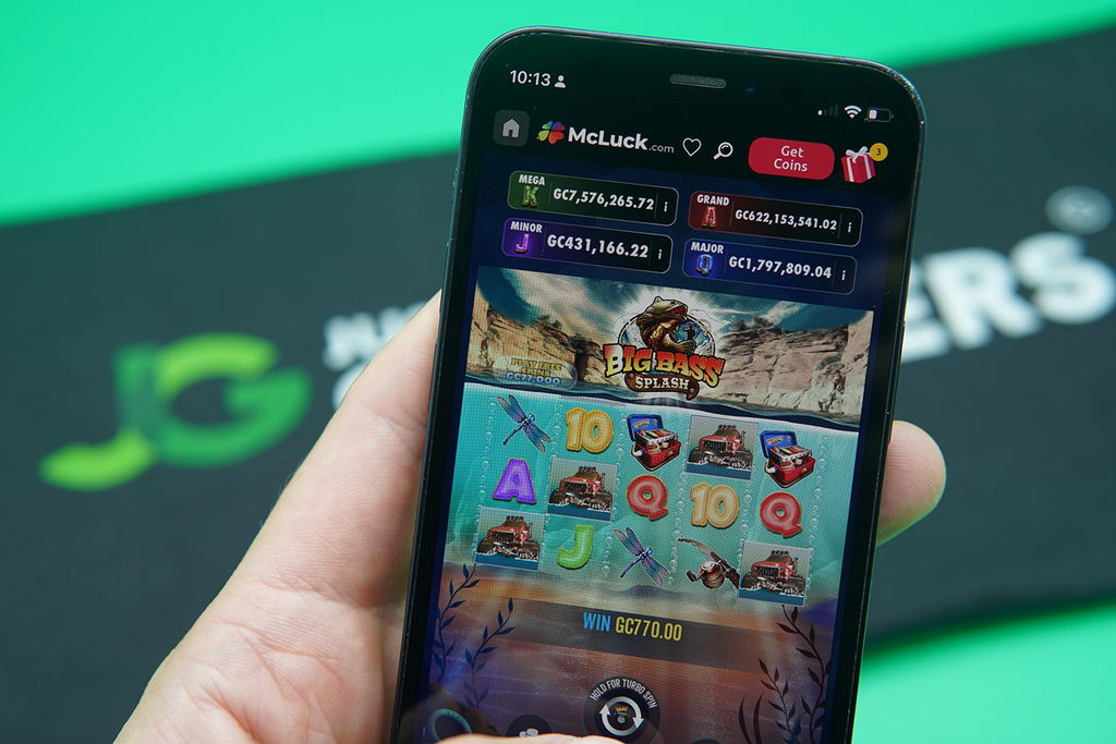 Patrik Lidin holding an iPhone with McLuck casino game Big Bass Splash showing.