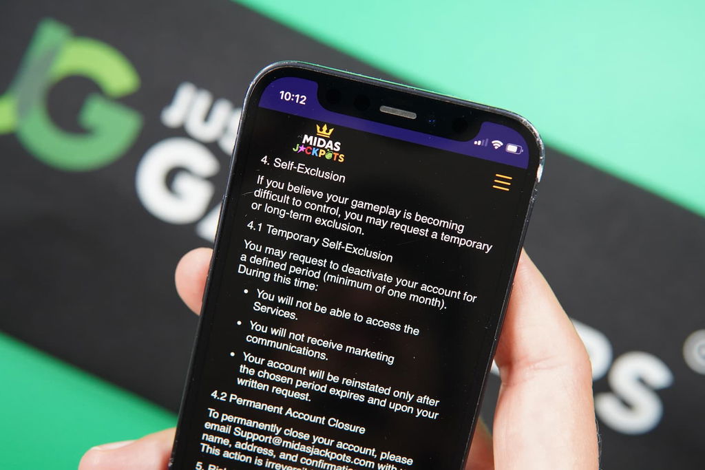 Patrik Lidin holding an iPhone with the Midas Jackpots casino responsible gaming page loaded on the webpage.