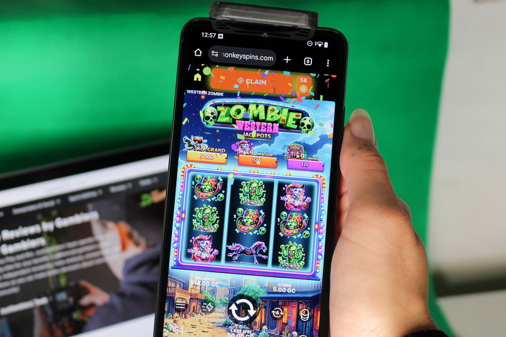 Angela Zillich holding an iPhone with the Monkey Spins casino mobile in-game page loaded on the webpage.