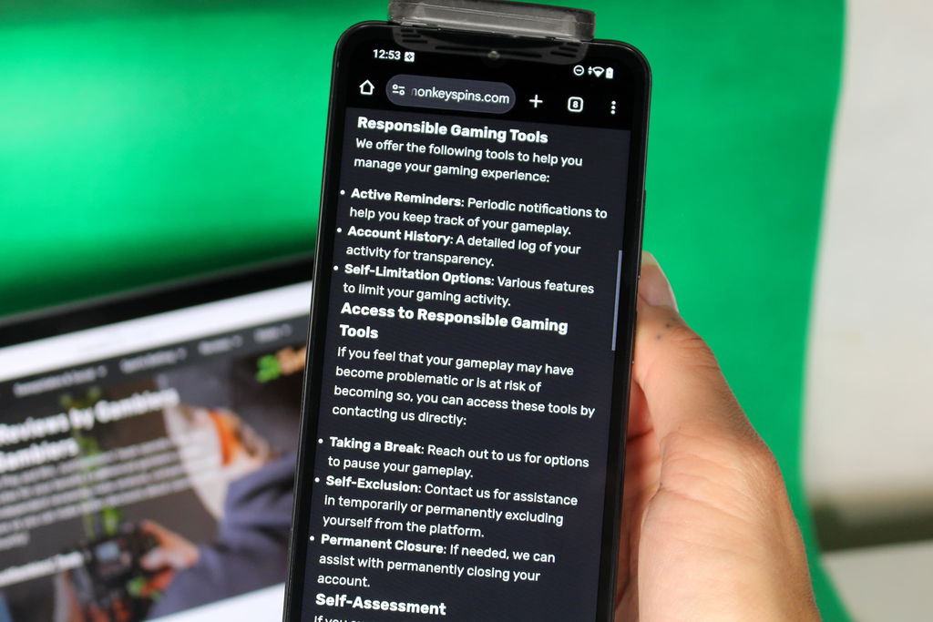 Angela Zillich holding an iPhone with the Monkey Spins casino Responsible Gambling page loaded on the webpage.