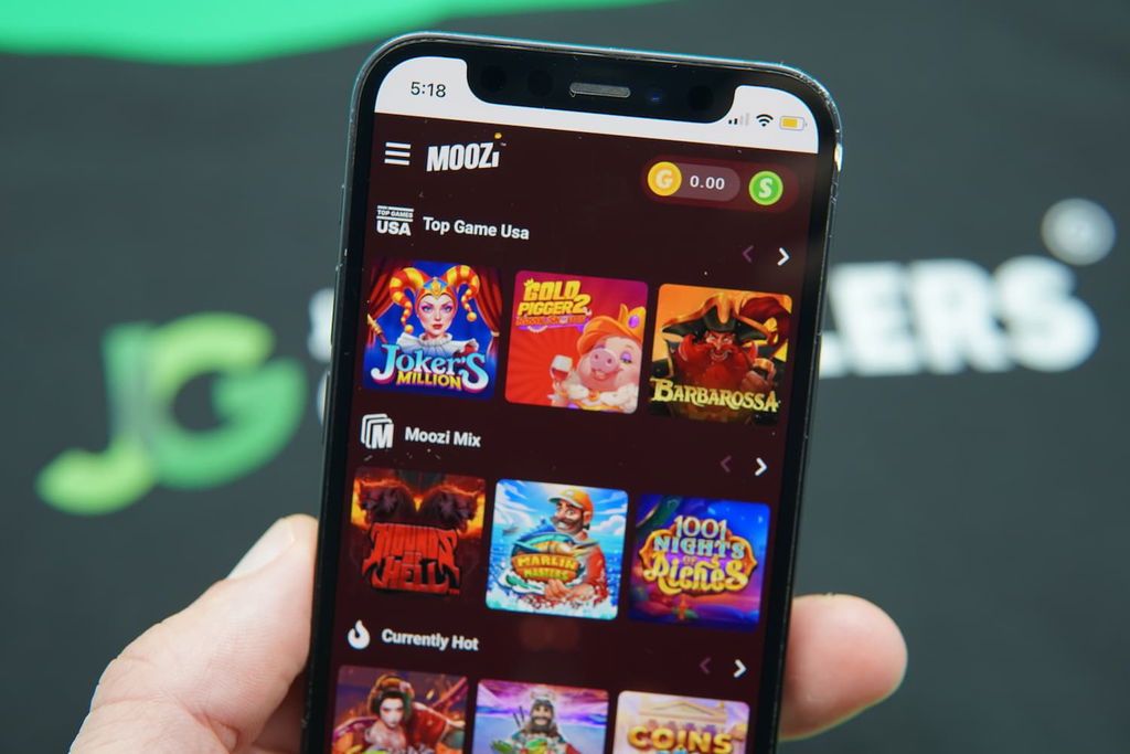 Patrik Lidin holding an iPhone with the Moozi casino game library page loaded on the webpage.