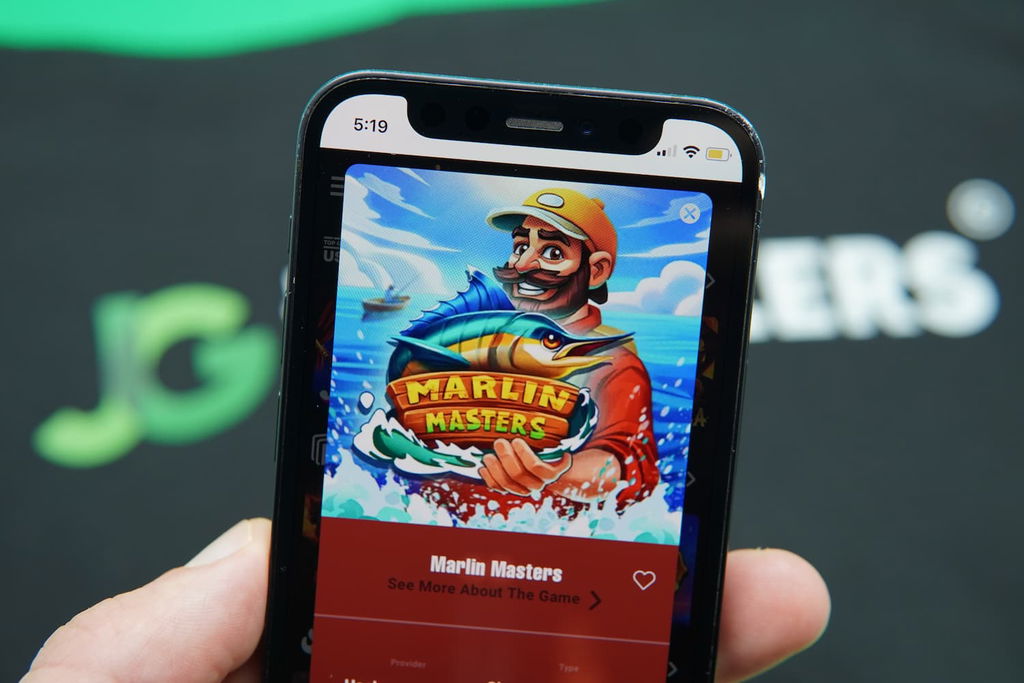 Patrik Lidin holding an iPhone with the Moozi casino mobile game page loaded on the webpage.