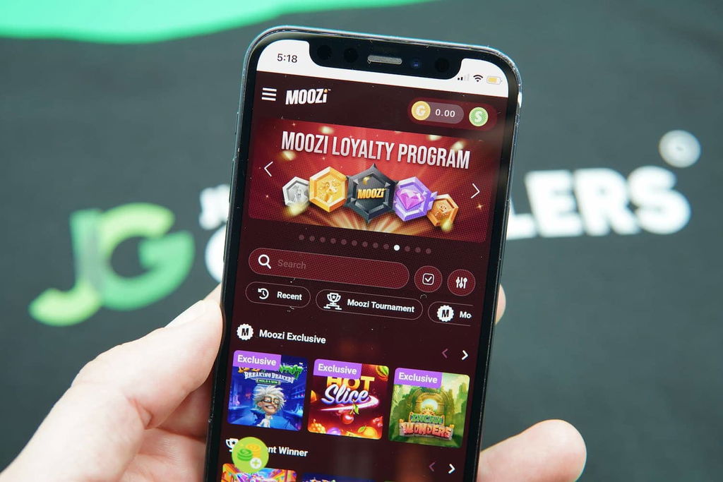 Patrik Lidin holding an iPhone with the Moozi casino landing page loaded on the webpage.