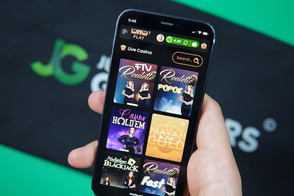 Patrik Lidin holding an iPhone with the Nioplay casino game library page loaded on the webpage.