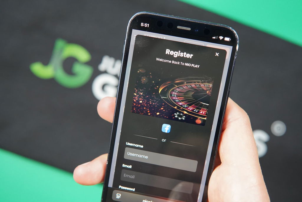 Patrik Lidin holding an iPhone with the Nioplay casino registration page loaded on the webpage.