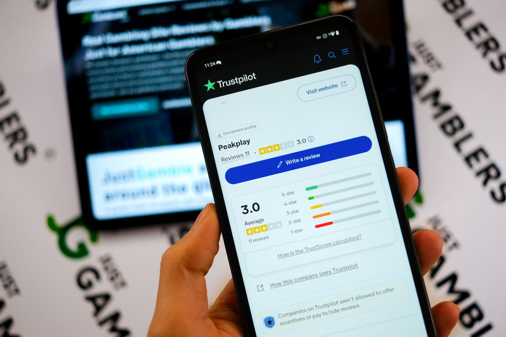 Angela Zillich holding an Android Phone with the PeakPlay casino Trustpilot page loaded on the webpage.