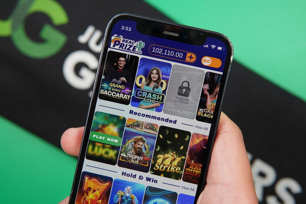 Patrik Lidin holding an iPhone with the RealPrize casino game library page loaded on the webpage.