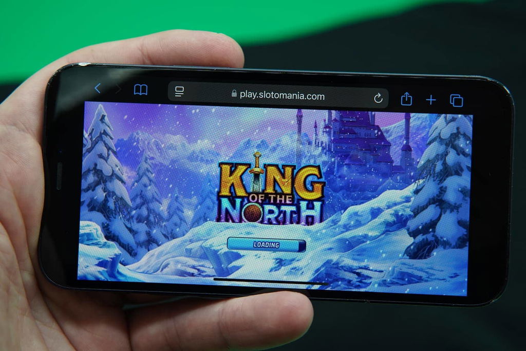 Patrik Lidin holding an iPhone with the Slotomania casino mobile slow loading time loaded on the webpage.