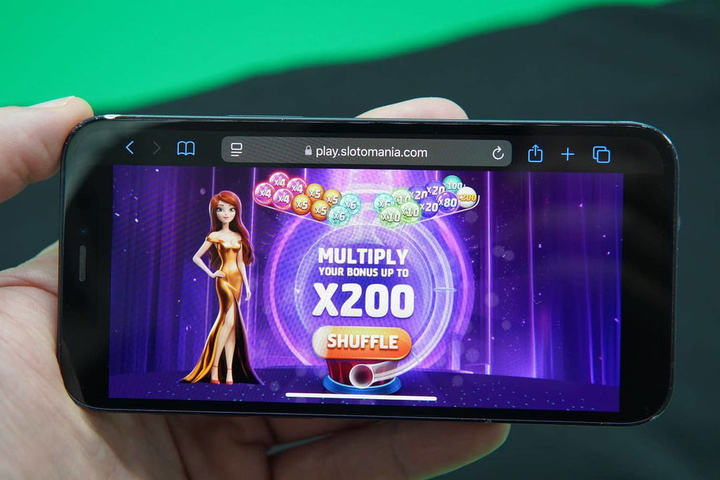Patrik Lidin holding an iPhone with the Slotomania casino promotions page loaded on the webpage.