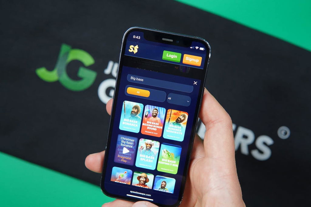 Patrik Lidin holding an iPhone with the SpeedSweeps casino game library scratch cards page loaded on the webpage.