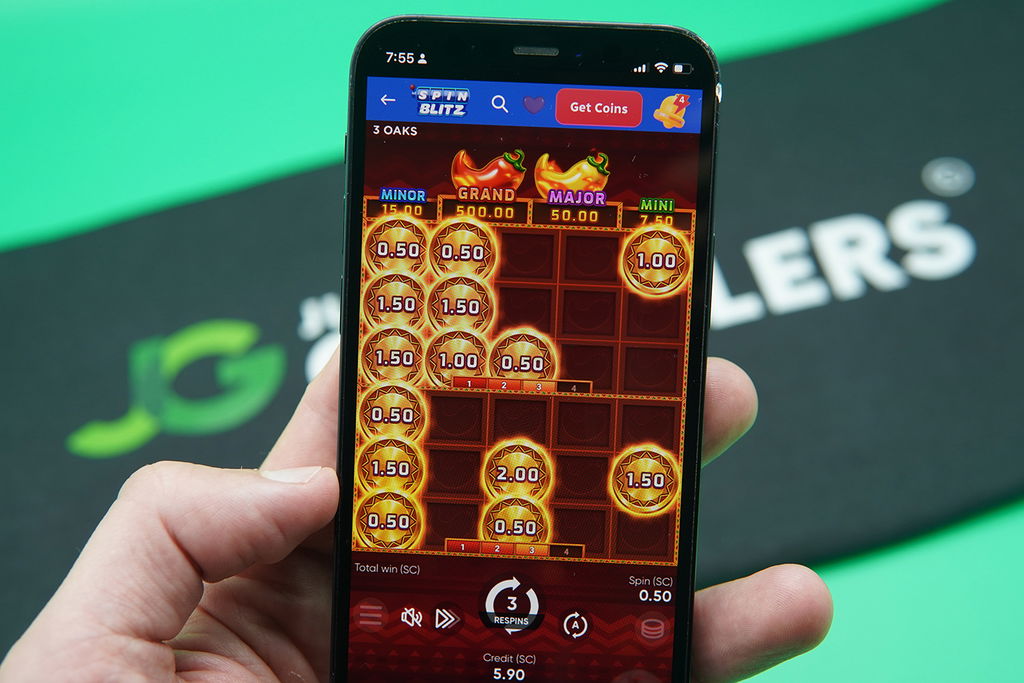 Patrik Lidin holding an iPhone with SpinBlitz casino game 3 Hot Chillies showing.