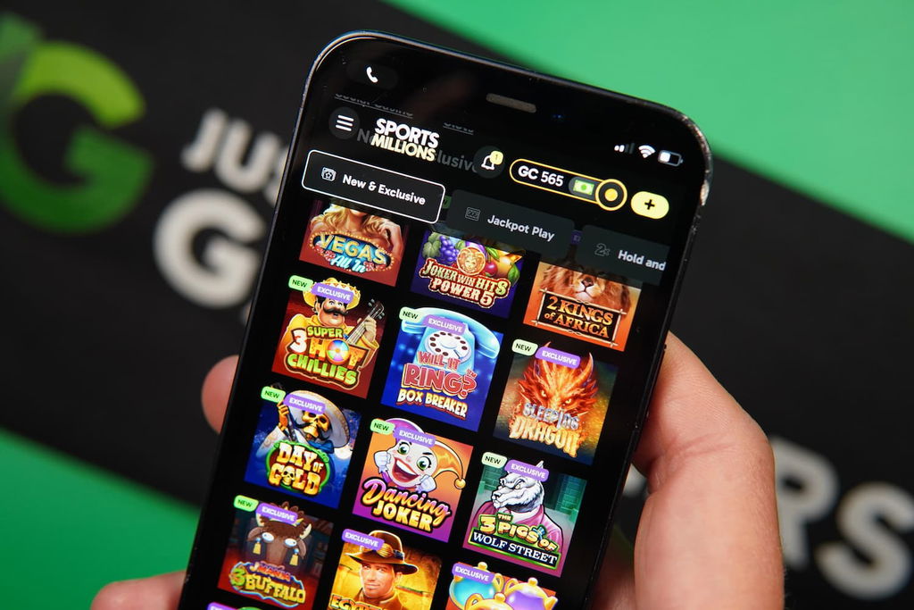 Patrik Lidin holding an iPhone with the Sports Millions sweepstakes casino game library page loaded on the webpage.