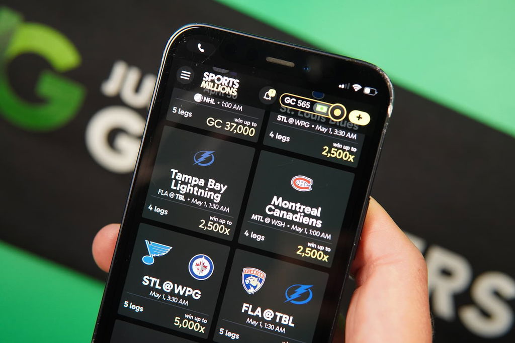 Patrik Lidin holding an iPhone with the Sports Millions sweepstakes casino sports predictions page loaded on the webpage.