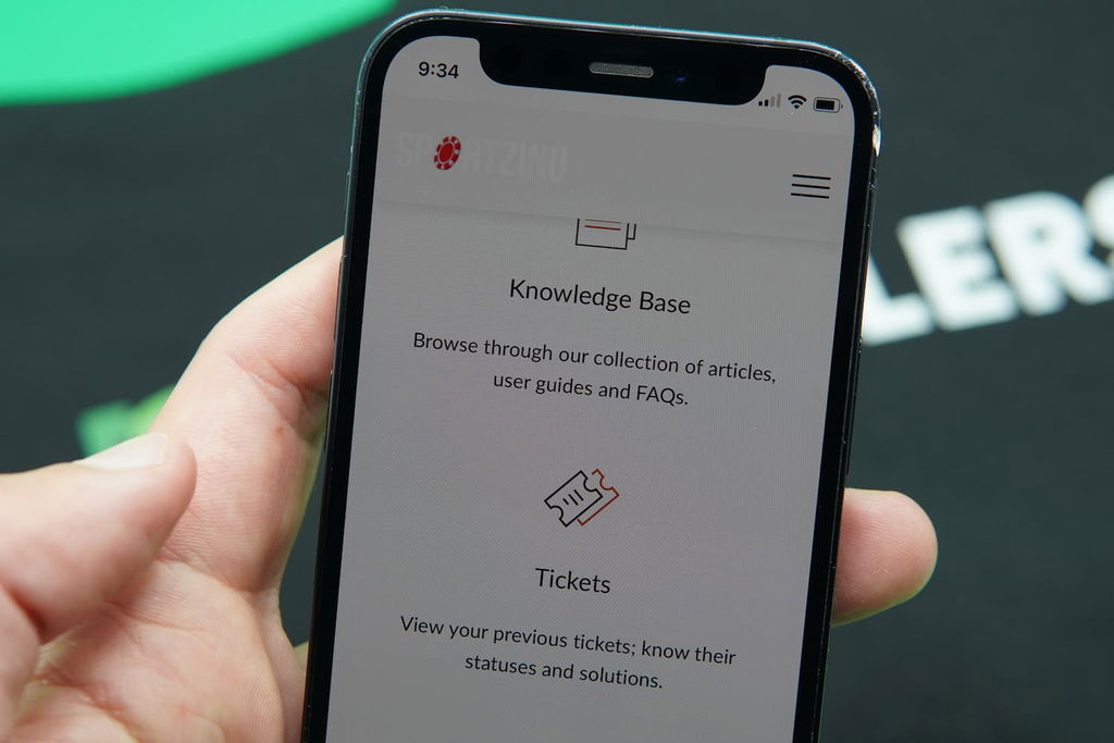 Patrik Lidin holding an iPhone with the Sportzino casino customer support page loaded on the webpage.
