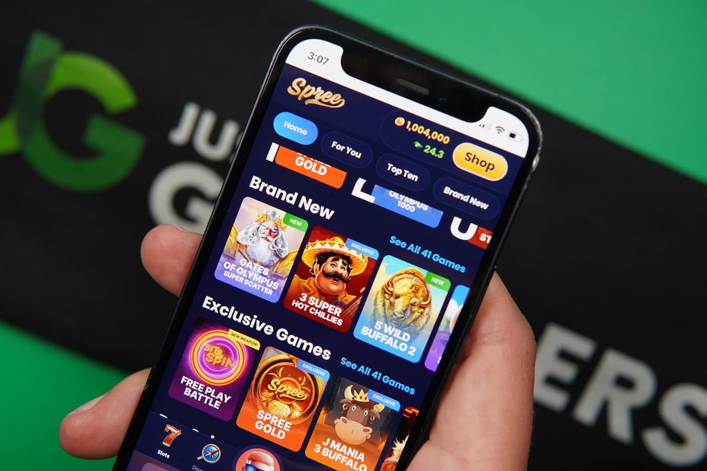 Patrik Lidin holding an iPhone with the Spree casino game library page loaded on the webpage.