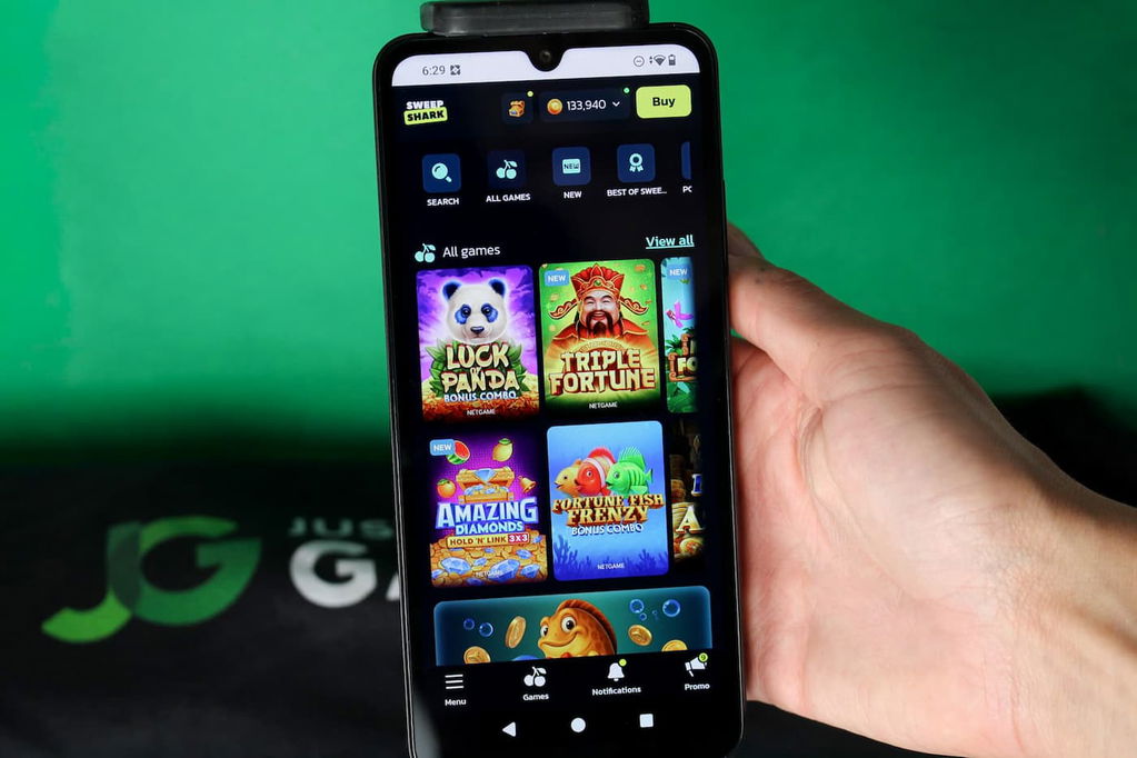 Angela Zillich holding an iPhone with the SweepShark casino gaming library page loaded on the webpage.