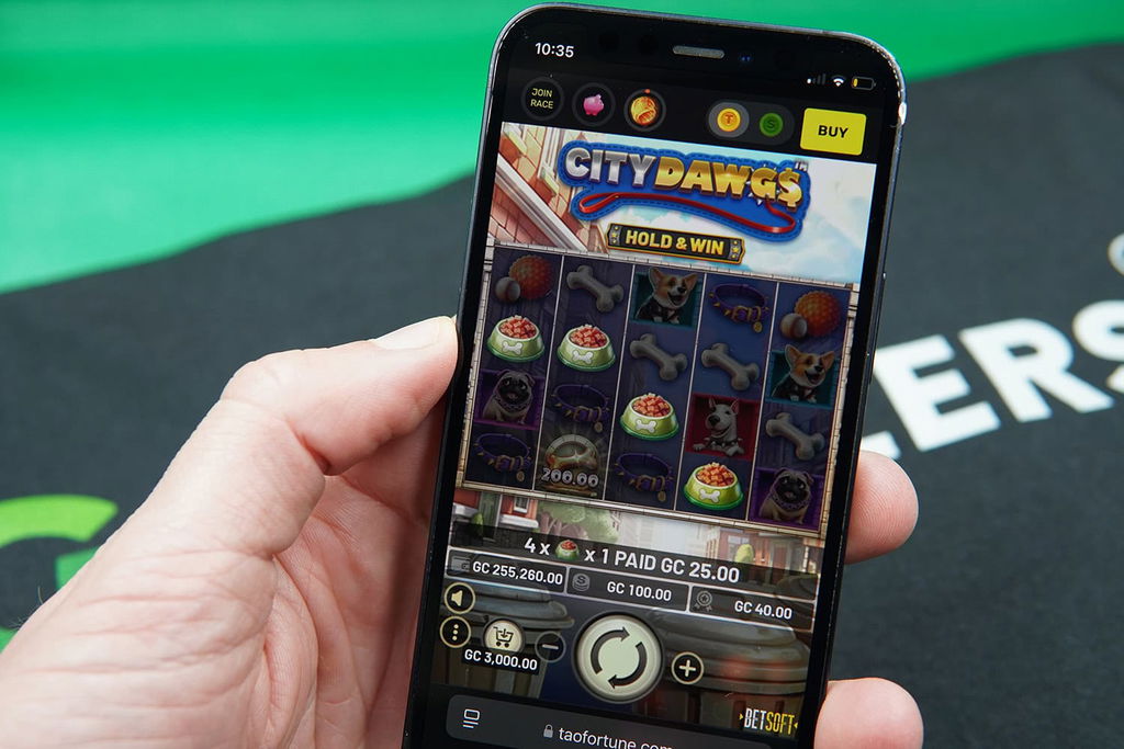 Patrik Lidin holding an iPhone with TaoFortune casino game City Dawgs showing.