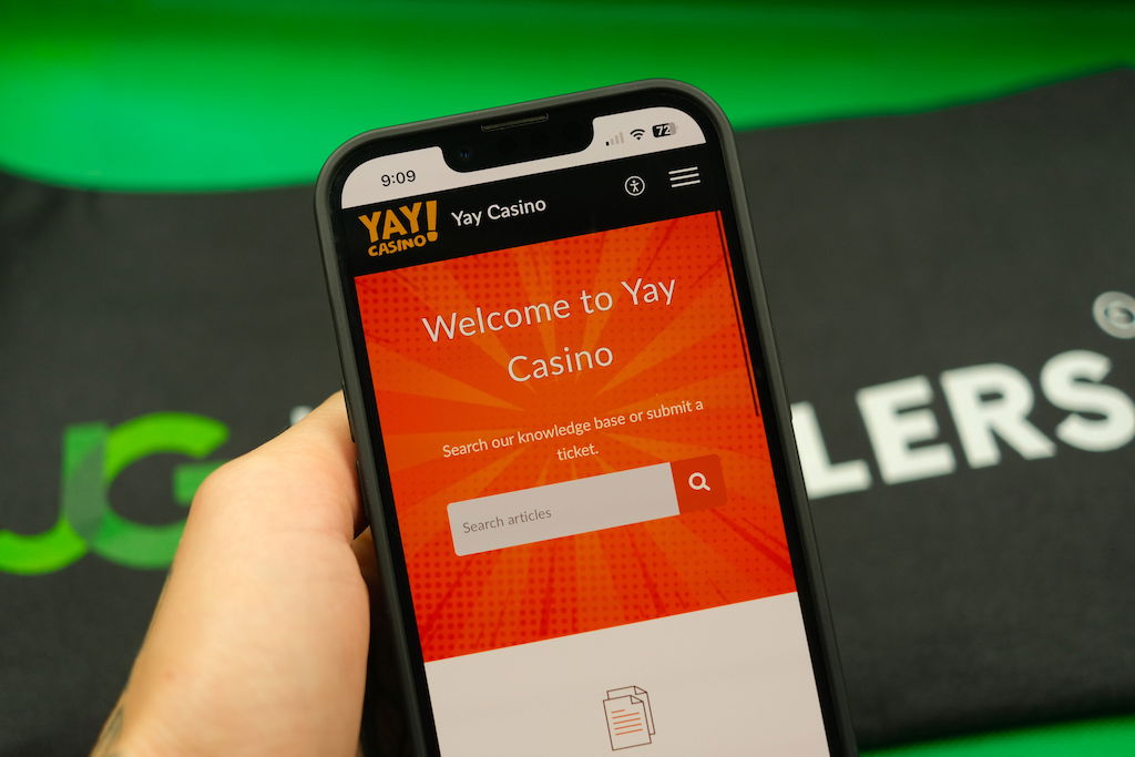 Patrik Lidin holding an iPhone with the Yay casino Help Center page loaded on the webpage.