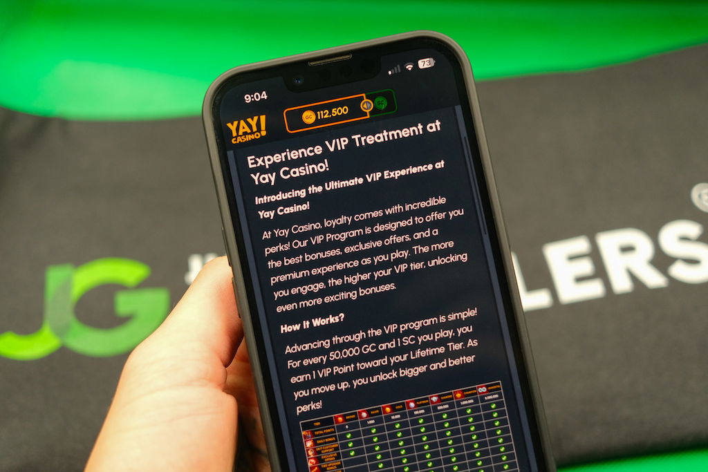 Patrik Lidin holding an iPhone with the Yay casino VIP Program page loaded on the webpage.