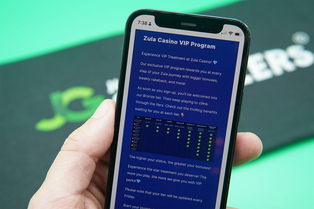 Patrik Lidin holding an iPhone with the Zula Casino VIP Program loaded on the webpage.
